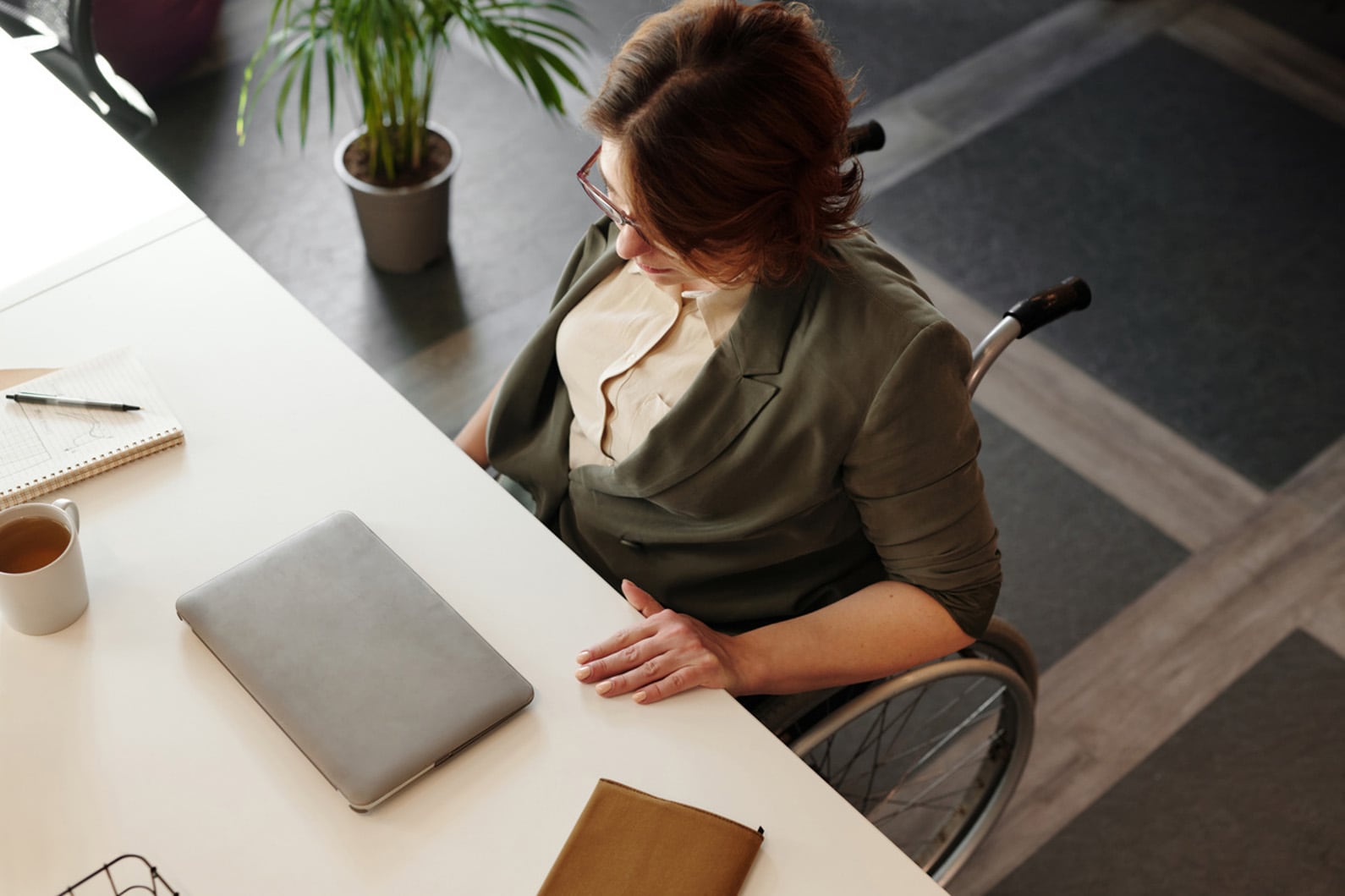A top view of a person on a manual wheelchair sitting in front of a desk looking down at a laptop