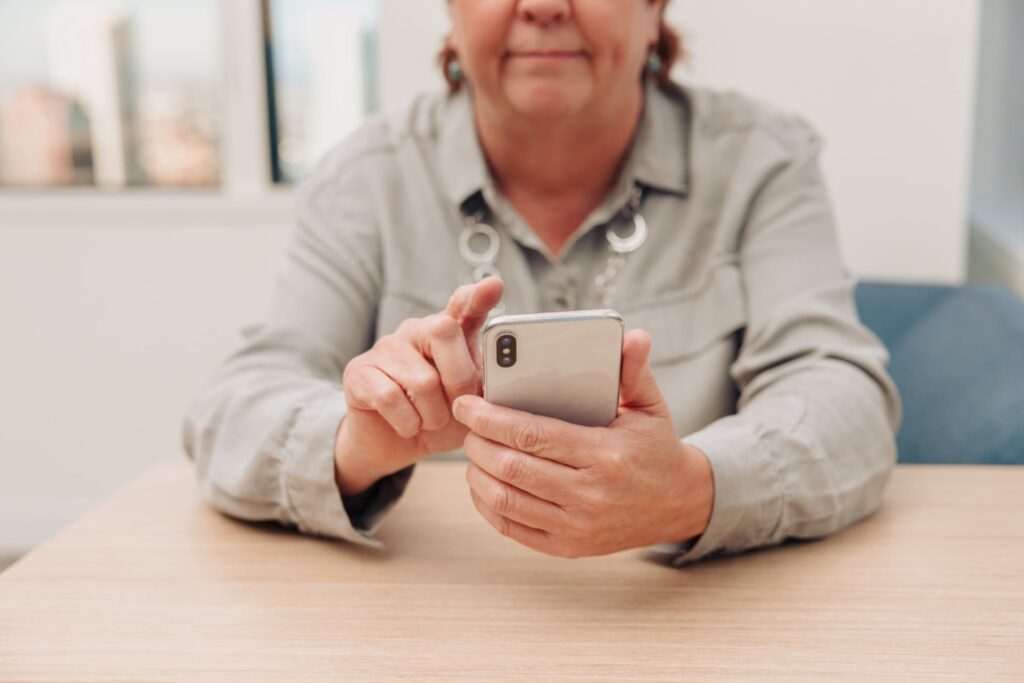 A front view of a woman sitting at a table holding her phone with one hand and using her other finger to touch the phone screen.