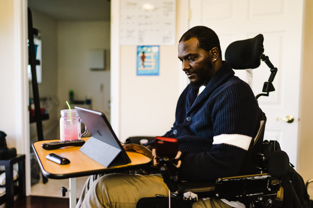 A sideview of a man in a wheelchair using a tablet and smartphone at a desk