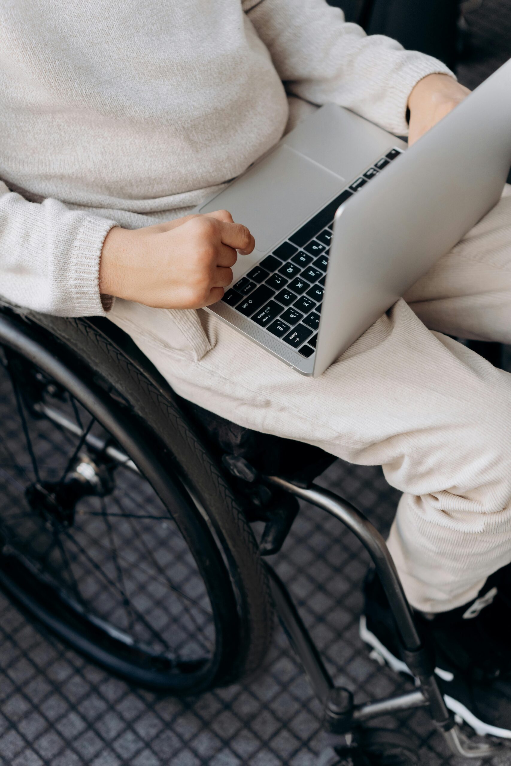 A top view of a person wearing a light-colored sweater, using a laptop with a close-up focus on the hands and the device